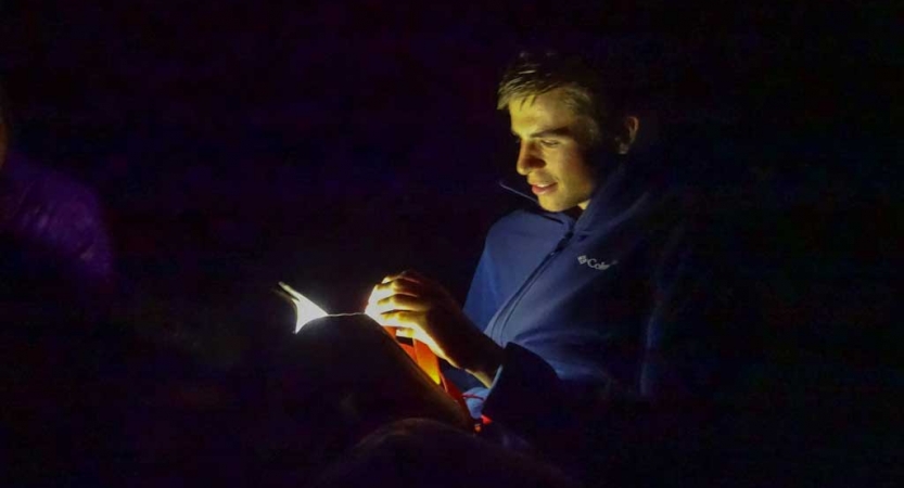 A person's face is illuminated by a flashlight as they read.